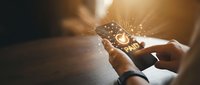 Hands holding smartphone with glowing paid confirmation screen, golden light particles, digital payment success concept for finance and technology.