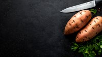 Fresh raw sweet potatoes with kitchen knife and parsley on black stone background with copy space for menu design and recipe text.