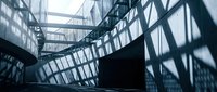 Modern office building interior with curved staircase and glass walls creating dramatic shadows and geometric patterns in corporate architecture space.