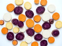 Colorful sliced root vegetables including purple cabbage, carrots, parsnips and turnips arranged on white background for healthy cooking and nutrition.