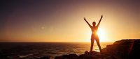 Silhouette of person with raised arms celebrating success on rocky cliff overlooking ocean at golden sunset, freedom and achievement concept for motivation.