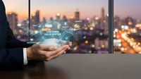 Businessman holding digital customer relationship management system interface with glowing icons above palm against blurred cityscape at sunset for business technology and enterprise solutions.