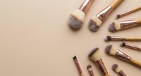 Professional makeup brushes with rose gold handles arranged on neutral beige background for beauty and cosmetics applications.