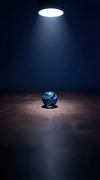 Glowing sphere with swirling blue and green patterns sits on wooden floor under bright overhead light in dark room, creating dramatic spotlight effect for concepts of focus, attention, and discovery.
