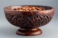 Ornate wooden carved bowl with intricate floral pattern filled with fresh almonds on gray background, traditional handcrafted decorative nutbowl for serving snacks.