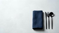 Dark blue linen napkin with black cutlery set on white textured surface, minimalist table setting for restaurant, catering, dining and hospitality design.