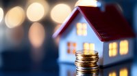 Glowing miniature house with stack of coins in foreground against blurred bokeh lights, representing real estate investment, mortgage and property finance.