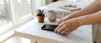 Caucasian man placing smartphone on wooden desk beside coffee mug and succulent plant in bright home office workspace.