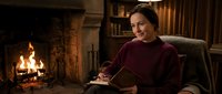 Young woman reading book by fireplace in cozy library setting with warm lighting and comfortable armchair creating peaceful evening atmosphere.