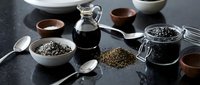 Black sesame seeds in glass jars and bowls with oil bottle on dark surface. Healthy cooking ingredients for Asian cuisine and natural wellness recipes.