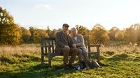 Senior couple sitting together on wooden bench in countryside during golden hour sunset enjoying peaceful retirement moment.