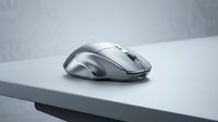 Wireless computer mouse in silver metallic finish positioned on white desk surface with gray background, suitable for technology and office design projects.
