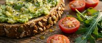 Whole grain toast topped with creamy avocado spread, fresh tomato slices, and microgreens on rustic wooden surface. Healthy breakfast or lunch option.