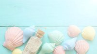 Pastel seashells and a small glass bottle with sand arranged on a mint wooden background, summer beach concept with copy space.