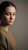 Young Caucasian woman in beige sweater with natural makeup and pulled back hair looking thoughtfully away from camera in soft studio lighting.