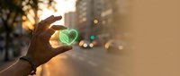 Hand holding green leaf with city street blurred in background at sunset, symbolizing environmental sustainability and eco-friendly urban living concepts.