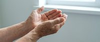 Elderly hands cupped together in prayer or receiving gesture showing aged skin with age spots in soft natural light for healthcare and spiritual concepts.