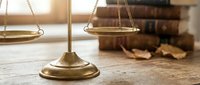 Golden brass scales of justice on wooden desk with law books in background representing legal system fairness and judicial balance in courtroom setting.