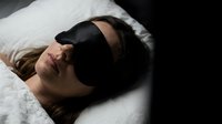 Young woman sleeping peacefully with black eye mask on white pillow in bedroom for rest and relaxation wellness lifestyle.