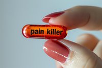 Female hand with red manicure holding transparent red capsule pill marked as pain killer against light background, medical and pharmaceutical concept.