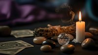 Mystical fortune telling setup with tarot cards, crystal ball, burning candle and sage bundle creating atmospheric divination scene for spiritual guidance practices.