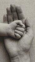 Tender moment of parent holding newborn baby hand in protective embrace, black and white photography capturing love, care and family bond connection.