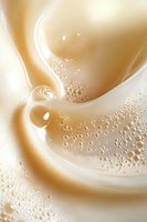 Creamy swirls and bubbles in soft beige and white tones create dynamic flowing abstract background with milky texture and gentle movement patterns.