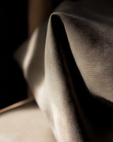Close-up macro shot of textured fabric with elegant folds and shadows creating abstract minimalist composition in neutral tones, suitable for luxury fashion marketing.