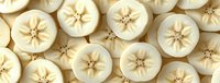 Fresh sliced bananas arranged in rows showing star pattern cross sections, natural organic fruit texture background in cream white and yellow tones.