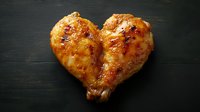 Grilled chicken breast shaped as heart on dark wooden background, glazed with honey marinade. Golden-brown, juicy meat with caramelized surface.