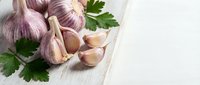 Fresh garlic bulbs and cloves with green parsley on rustic wooden cutting board. Organic cooking ingredients for healthy Mediterranean cuisine and recipes.