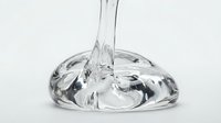 Transparent liquid pouring into clear glass bowl against white background, isolated design element suitable for beverage, cosmetics, and product packaging mockups.