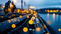 Blurred golden bokeh lights create dreamy atmosphere on wet surface during blue hour, with reflective water and urban lights in background, moody evening cityscape.