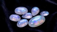 Collection of polished rainbow moonstone gems displaying iridescent blue flash adularescence on dark fabric background for jewelry making and gemology.