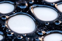 Macro photography of water drops forming circular patterns on dark hydrophobic surface, creating abstract geometric composition with light reflections.