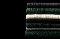 Stack of folded knitted sweaters in dark green, black, and cream tones on a dark background, cozy autumn winter fashion concept.