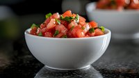 Fresh watermelon salad with chopped herbs in white ceramic bowl on dark background, selective focus. Summer refreshing healthy food preparation.