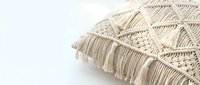 Handmade macrame cushion with intricate knotted pattern and fringe tassels on white background, boho home decor accent for living room styling.