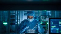 Male surgeon in sterile scrubs and mask performing precision surgery in modern operating room with advanced medical equipment and monitoring systems.