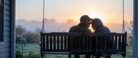 Romantic couple silhouettes sitting close together on porch swing during golden sunset hour creating intimate peaceful moment for love relationship concepts.