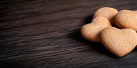 Heart shaped sugar cookies dusted with powdered sugar arranged on dark wooden background with copy space, romantic food photography for Valentine's Day or love concept.