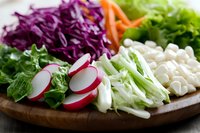 Fresh colorful vegetables arranged on wooden board including purple cabbage, radish, lettuce, carrots and cauliflower, macro food photography in natural light.