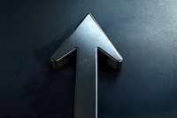 Metallic silver arrow pointing upward on dark background with dramatic lighting and shadow effect, symbolizing growth, success and forward momentum.