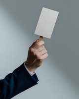 Male hand in business suit sleeve holding up blank white card against gray background. Professional gesture showing empty mockup space for business design.