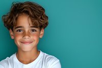Cheerful mixed race boy with curly hair wearing white t-shirt smiling confidently against turquoise background, copy space for text on right side.