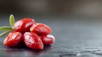 Fresh red goji berries with green leaves on dark wooden surface. Superfood antioxidant nutrition for healthy diet and wellness lifestyle concepts.