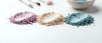 Colorful crushed eyeshadow powder makeup cosmetics in purple beige and teal shades scattered on white background for beauty and fashion concepts.