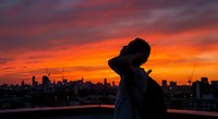 Young African American woman silhouette against vibrant sunset sky over city skyline. Urban lifestyle portrait for wellness and mindfulness content.
