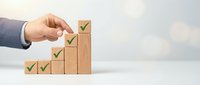 Businessman hand placing wooden blocks with green checkmarks in ascending steps representing business growth, success milestones and achievement progress.