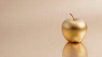 Golden apple with stem on reflective surface against soft beige background, symbolizing luxury, wealth, and achievement.